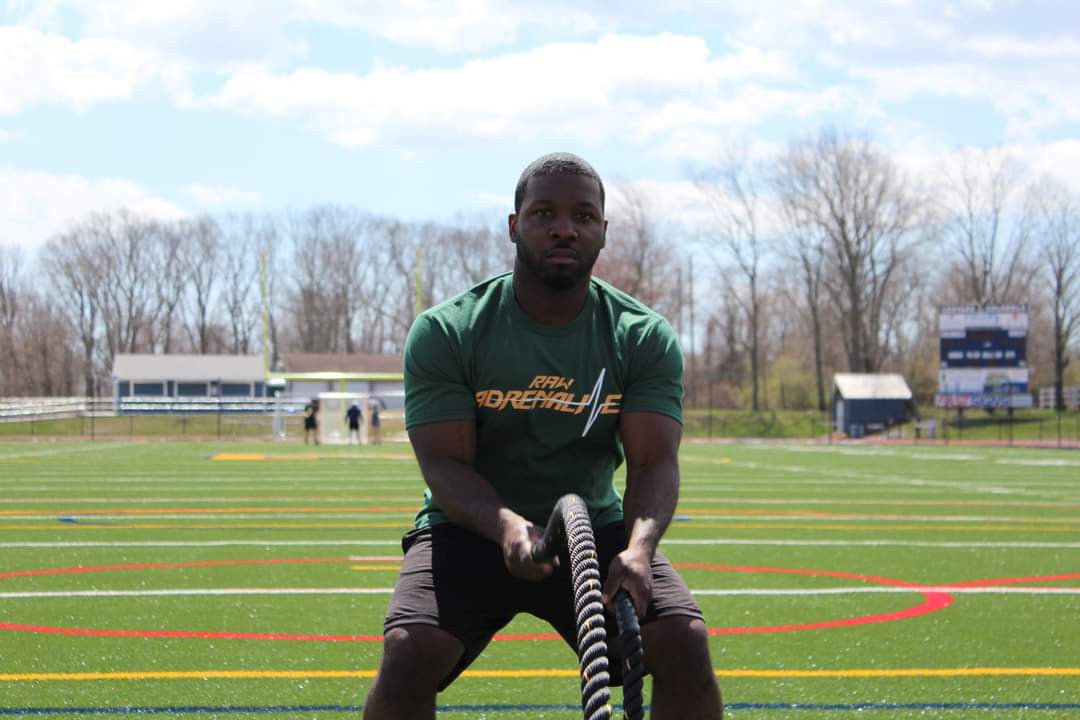 Person wearing a green Raw Adrenaline T-shirt using battle ropes outdoors.