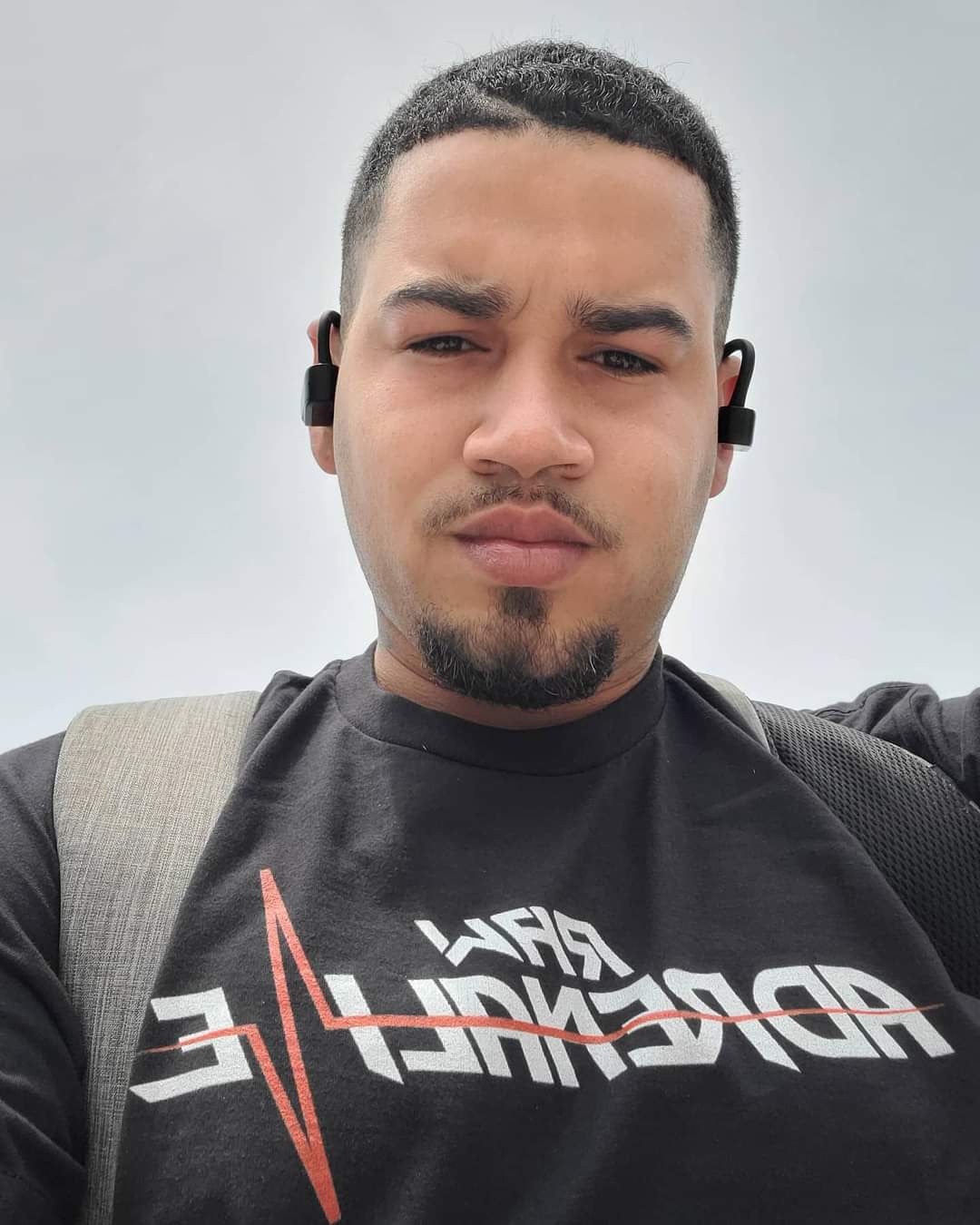 Outdoor selfie of a person wearing a black Raw Adrenaline T-shirt and a backpack.