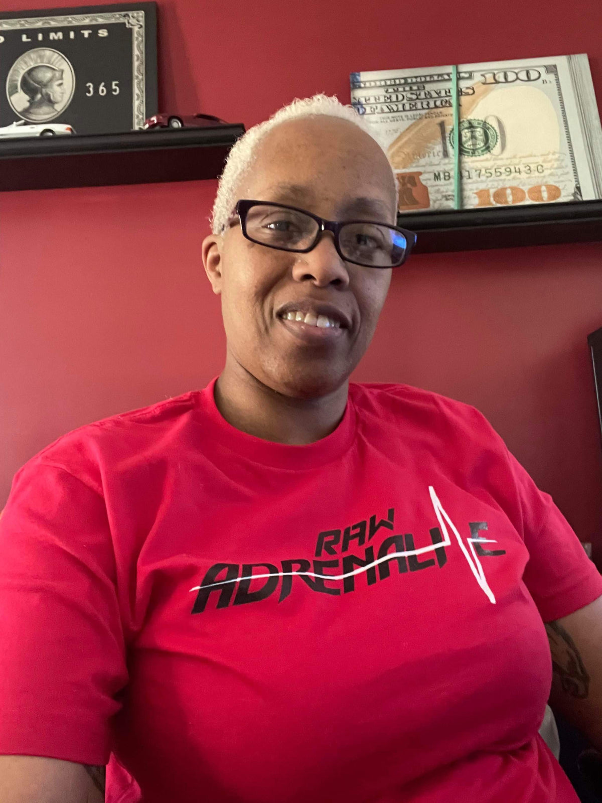 Smiling person wearing glasses and a red Raw Adrenaline T-shirt.