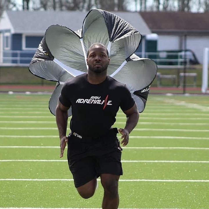 Runner wearing a black Raw Adrenaline T-shirt while training with a resistance parachute on a field.
